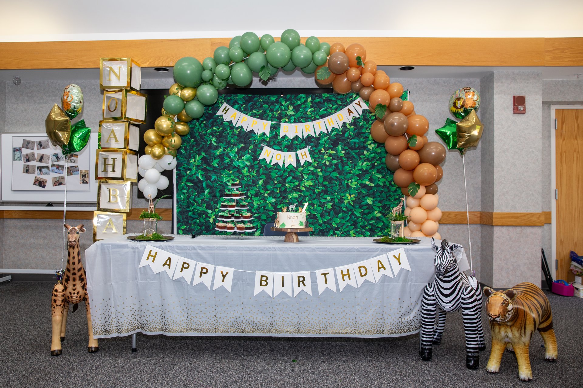 Safari jungle themed first birthday with balloon arch, greenery backdrop, and animal props